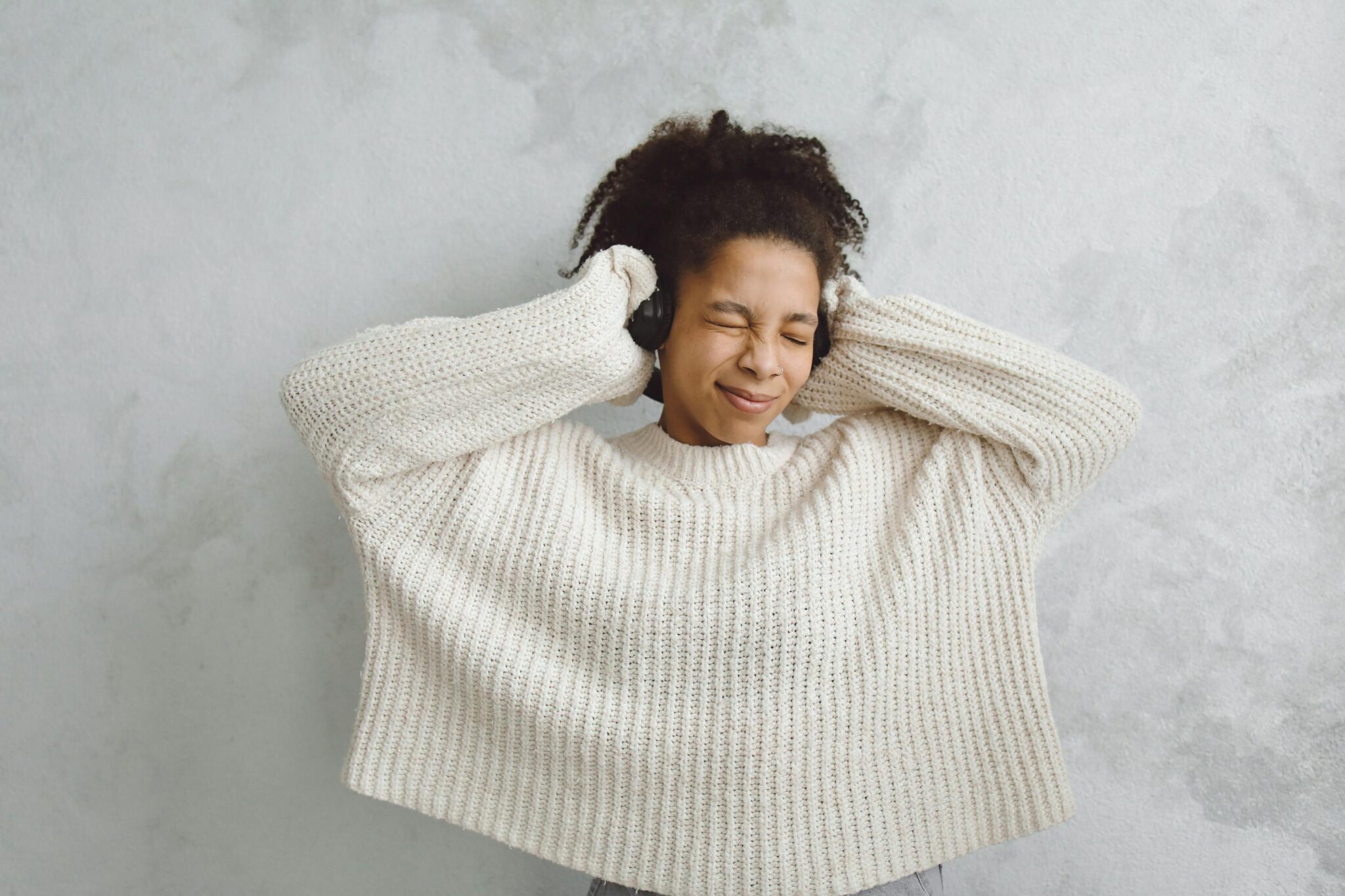 A woman with curly hair, eyes closed, enjoying music. Studio shoot in a knitted sweater.